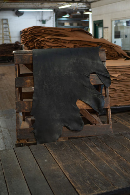 Black Skirting Leather from Hermann Oak Leather Co displayed on a wooden rack