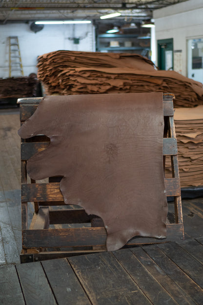 Dark Chocolate Skirting Leather from Hermann Oak Leather Co displayed on a wooden rack